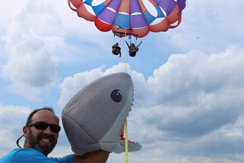 A person holding a large shark-shaped object with a parachute above. 4