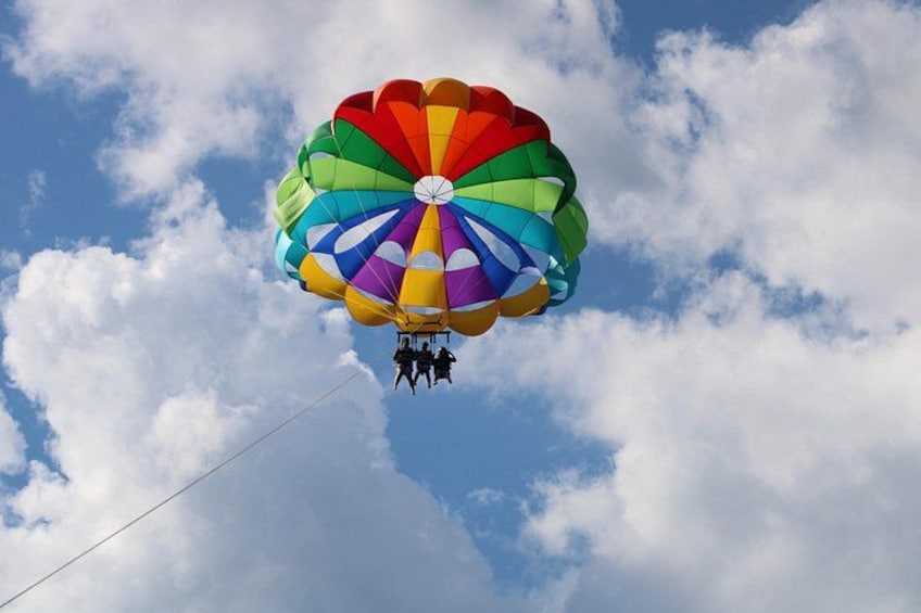 A colorful parachute with people attached, descending against a backdrop of clouds. 1