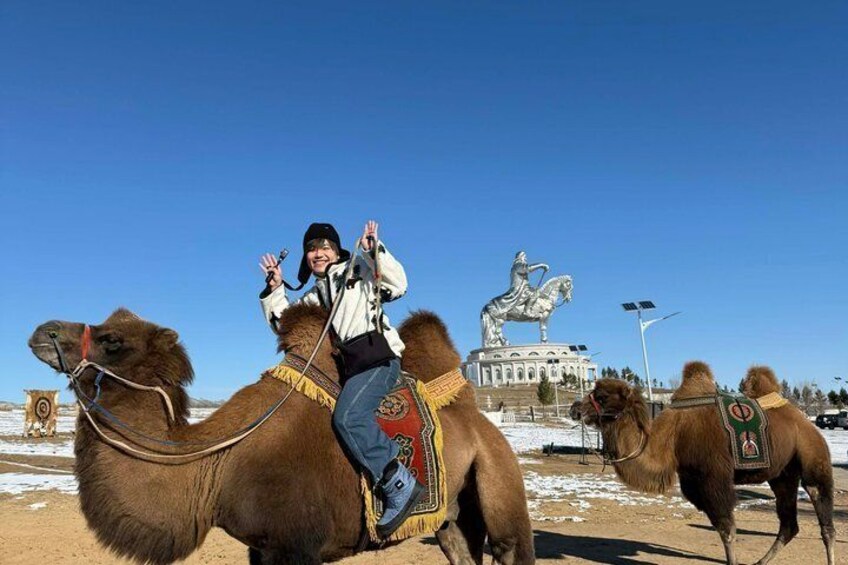 A person riding a camel with a statue in the background. 2