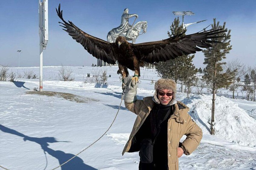 A person holding a large bird of prey with outstretched wings in a snowy landscape with trees and a clear sky. 4