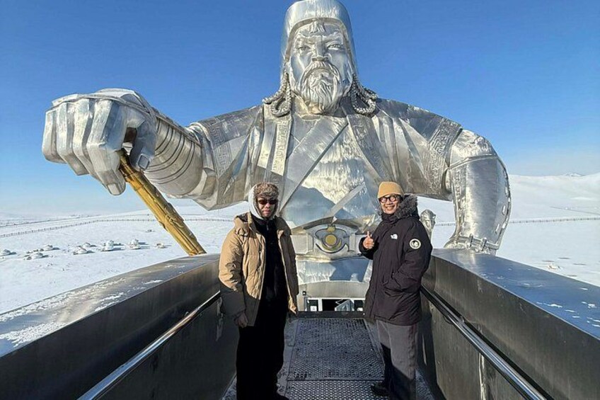Two people standing on a metal platform with a large metallic statue of a man in the background. 3