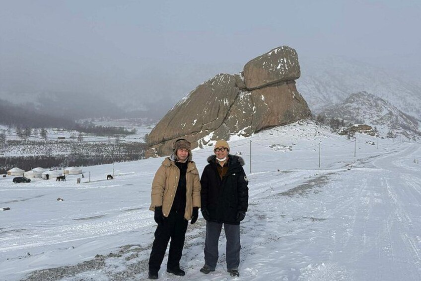 Two people standing on a snow-covered road with a large rock formation in the background. 5
