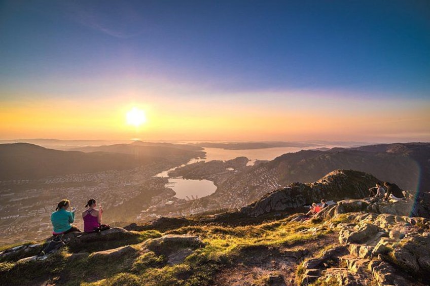 Een zonsondergang boven een bergachtig landschap met een meer en een groep mensen die op rotsen zitten. 1