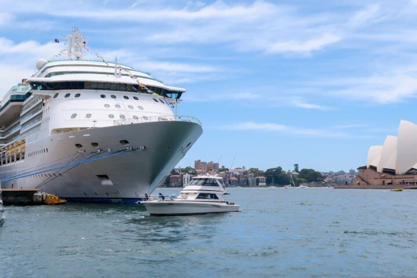 Een groot cruiseschip afgemeerd in de buurt van een stads haven, met een opvallend operagebouw op de achtergrond. 4