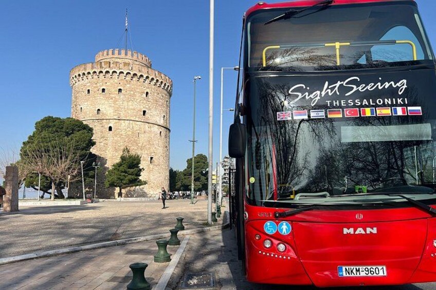 A red bus with 'Sightseeing Thessaloniki' on the front, parked in front of a historic stone tower. 2