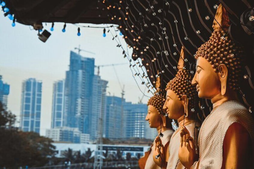 Tres estatuas de Buda con las manos en posición de oración, frente a un paisaje urbano con edificios altos. 4