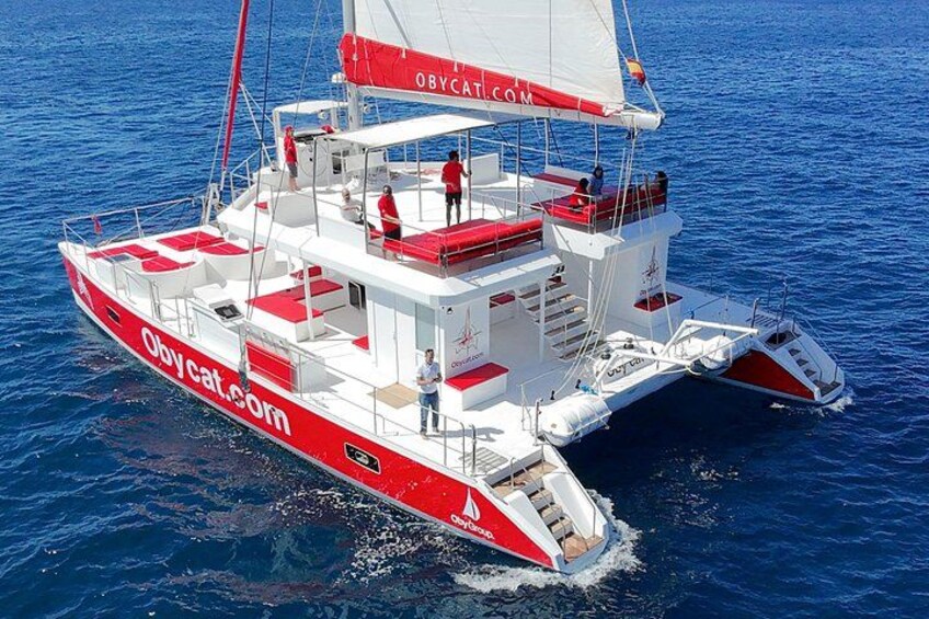 A red and white catamaran with the website 'obycat.com' on its side, sailing on blue water. 2