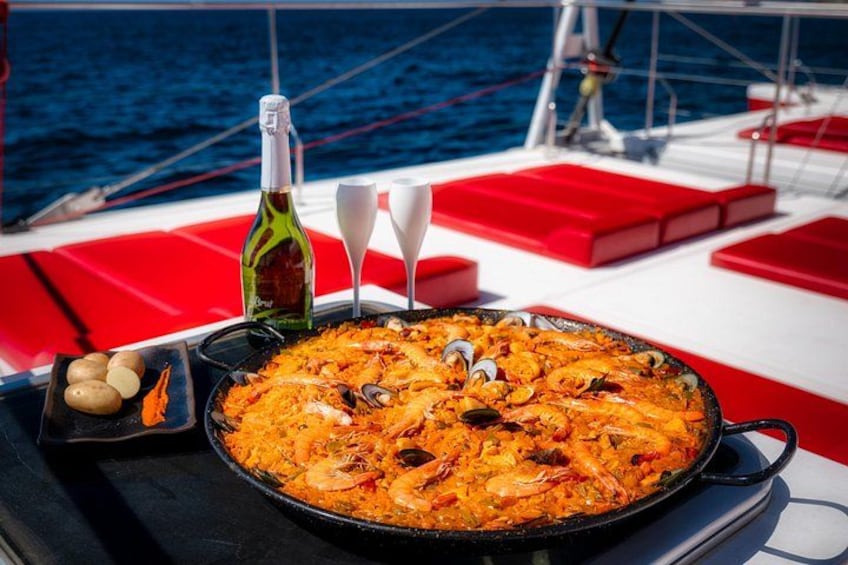 A seafood paella on a boat with red seating and a bottle of wine. 2