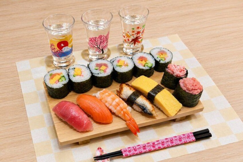 Sushi su un tagliere di legno, con nigiri e involtini maki, bacchette e piccoli bicchieri d'acqua. 1