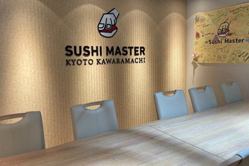 Una sala riunioni con un lungo tavolo e quattro sedie, una parete con il testo 'SUSHI MASTER KYOTO KAWARAMACHI' e un logo, e una mappa con lo stesso testo. 3