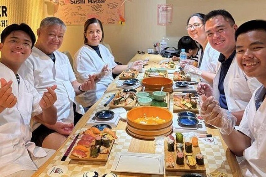 Un grupo de personas sentadas alrededor de una mesa larga con diferentes platos de sushi. 2