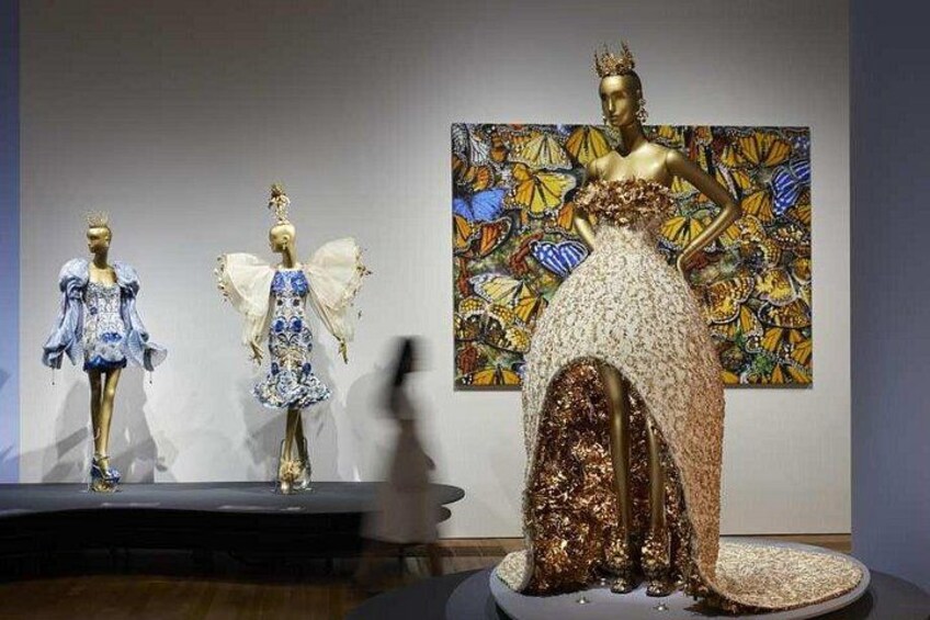 Tres maniquíes con vestidos elaborados, uno con una corona, frente a un colorido telón de fondo pictórico. 4