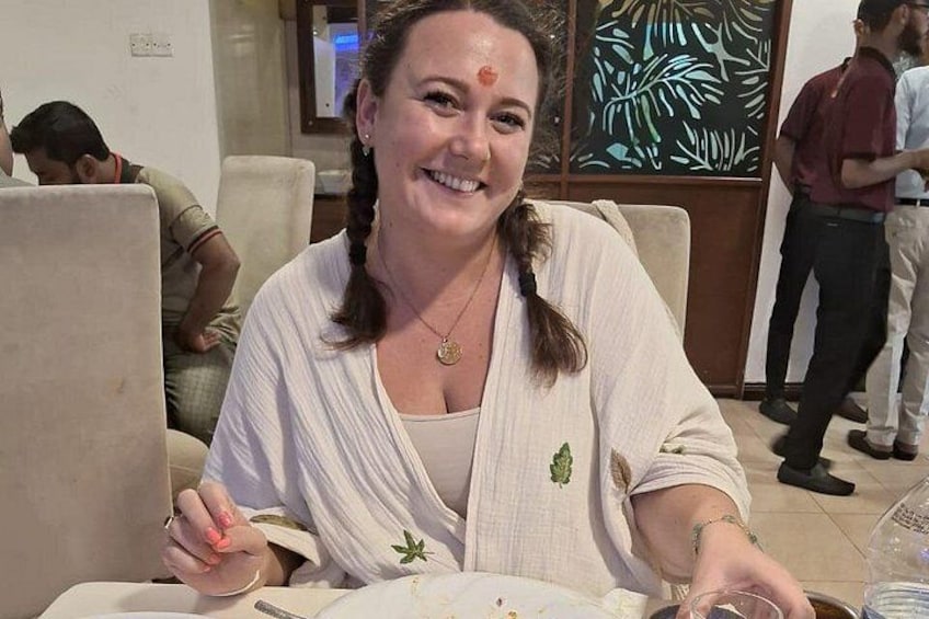 A person sitting at a table with a plate and utensils, in a room with other people in the background. 4