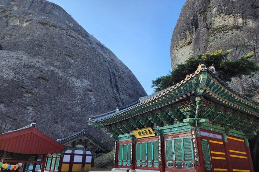 A traditional Korean temple with a large rock formation in the background. 4