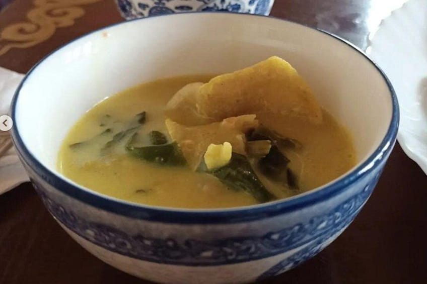 A bowl of soup with vegetables and a piece of meat, served in a blue and white patterned bowl. 2