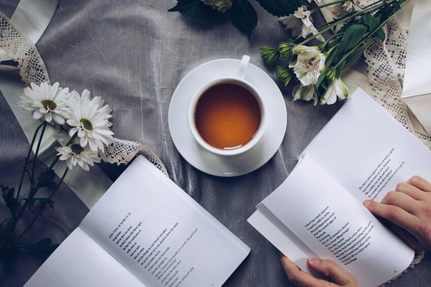 A cup of tea, two open books, and white flowers on a table. 2