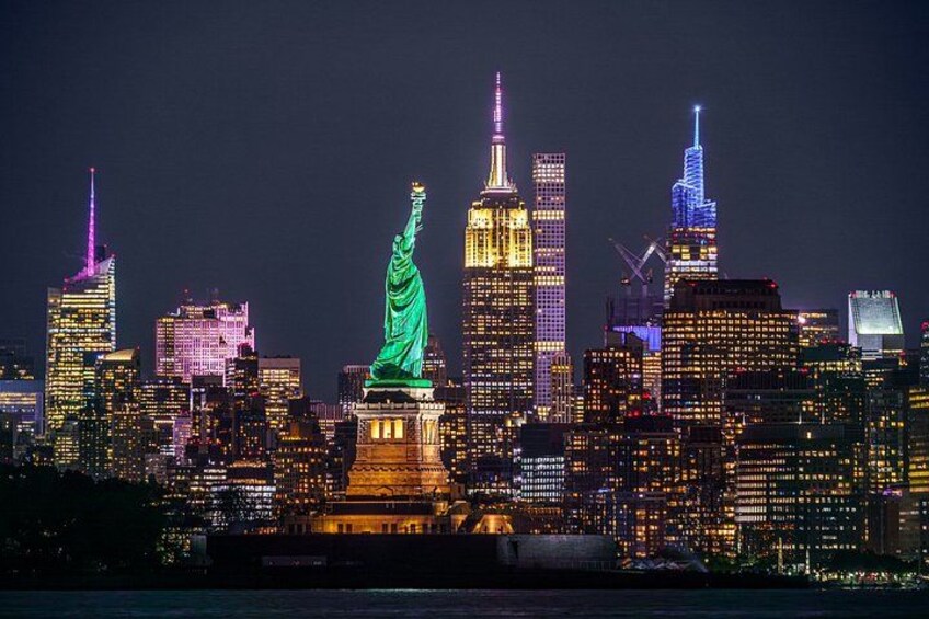 La silhouette de New York la nuit, avec la statue de la Liberté illuminée en vert, l’Empire State Building et d’autres gratte-ciel. 1