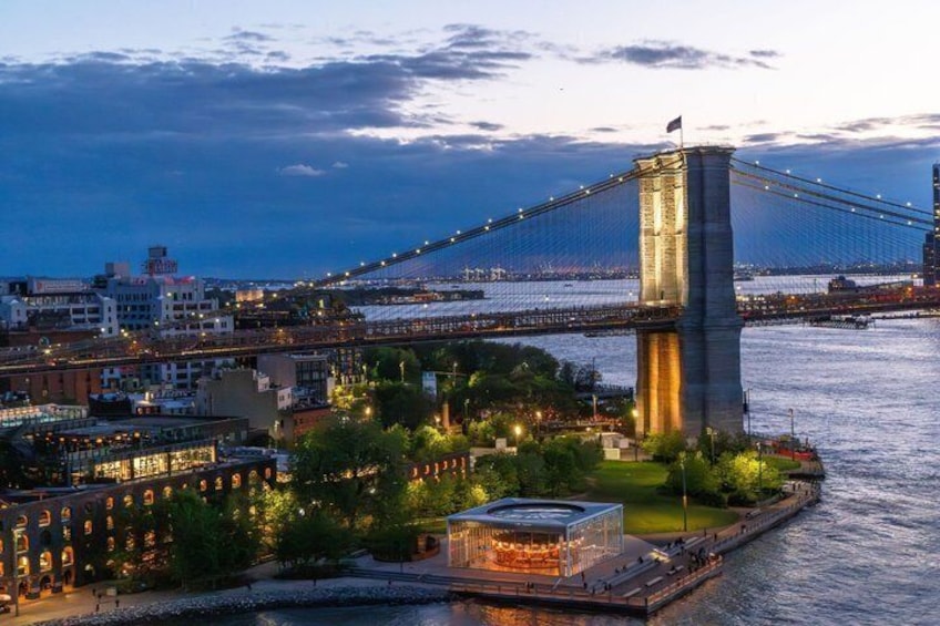 A suspension bridge with a central tower, a river, and a cityscape with buildings and greenery. 2