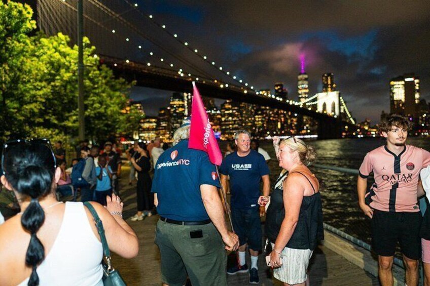 A group of people walking along a waterfront with a bridge and city skyline in the background. 3