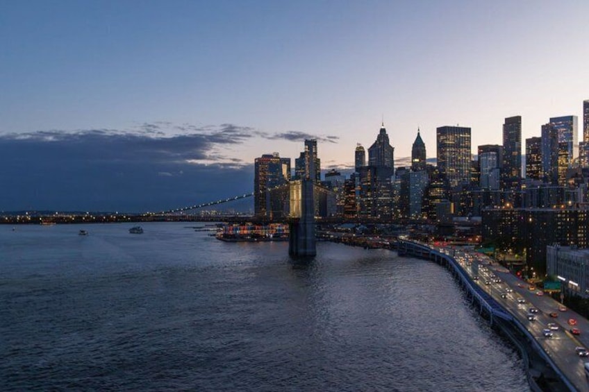 A city skyline at dusk with a prominent bridge crossing a river, surrounded by high-rise buildings. 3