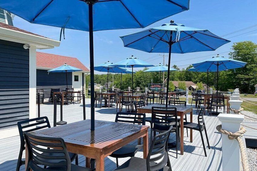 Una terrazza esterna con tavoli e sedie in legno, ombrelloni blu e un pontile in legno. 2