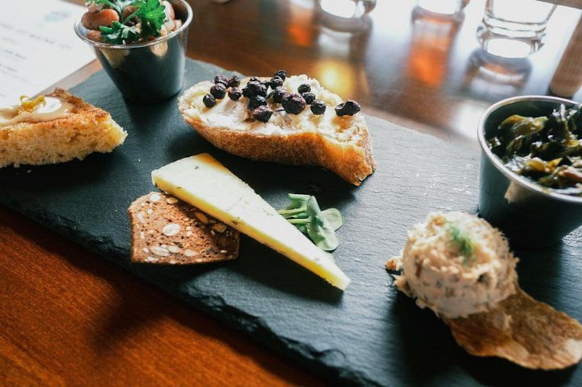 A variety of food items on a slate board, including bread with toppings, a slice of cheese, and a bowl of greens. 2