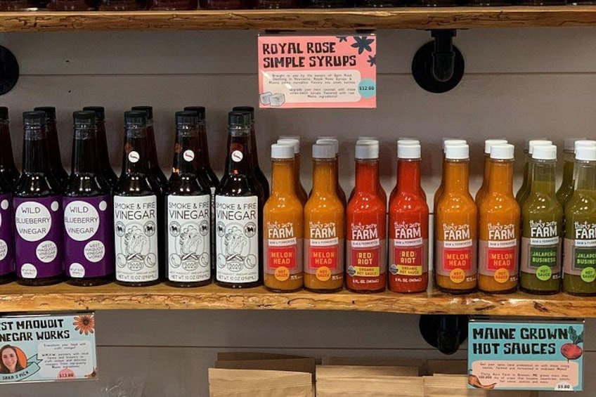 A shelf with various bottles of vinegar and hot sauces, including labels like 'Wild Blueberry Vinegar' and 'Smoke & Fire Vinegar.' 1