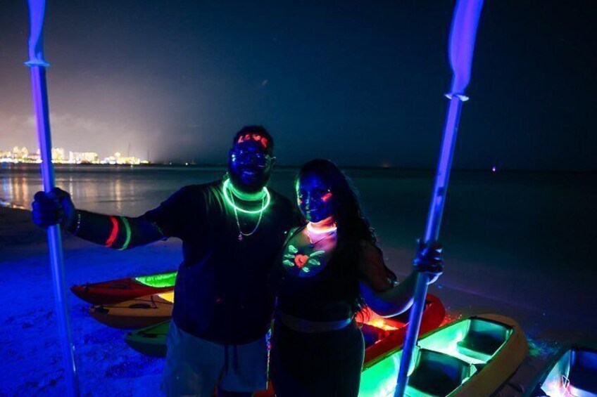 Two people standing on a beach at night with glow sticks and a kayak. 4