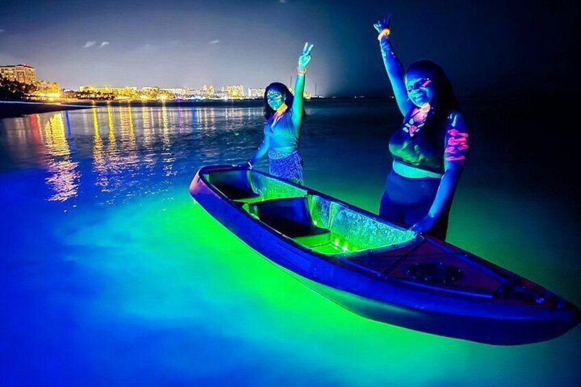 Two people in a boat on a body of water at night with city lights in the background. 1