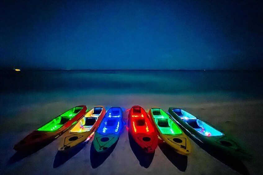 Six kayaks lined up on a beach at night with colorful lights. 5