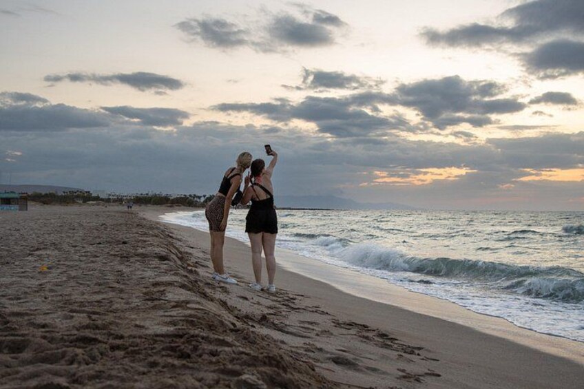 A beach with two people taking a selfie, the ocean, and a cloudy sky. 5