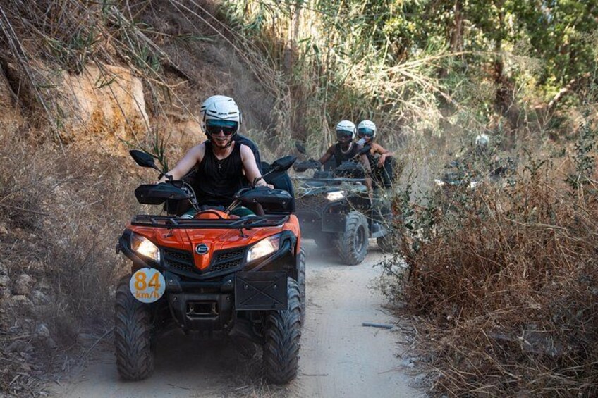 Two people riding ATVs on a dirt path surrounded by dry vegetation. 4