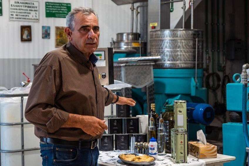 A man in a checkered shirt standing in a kitchen with industrial equipment, pointing at a table with bottles and a pie. 2
