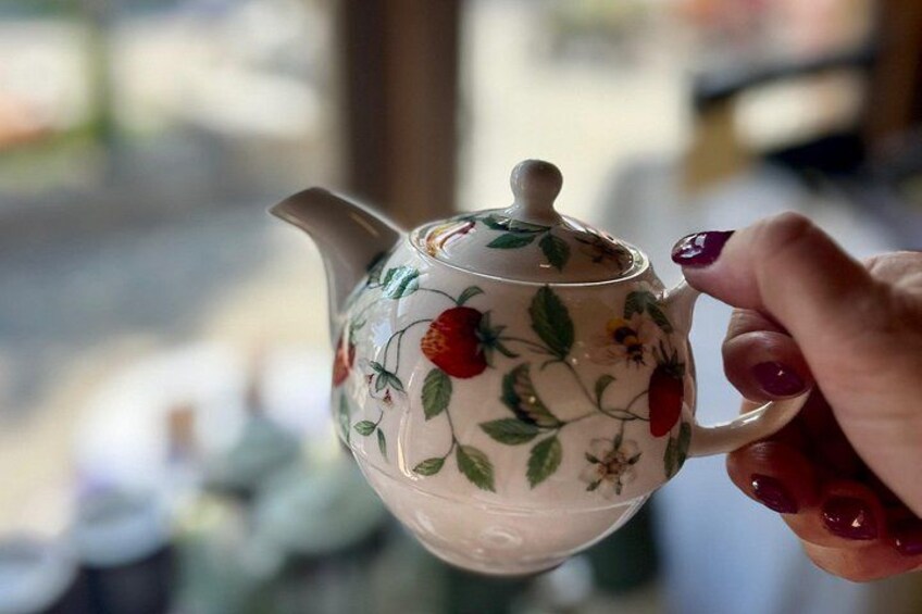 Una mano sostiene una tetera con motivos florales. 4