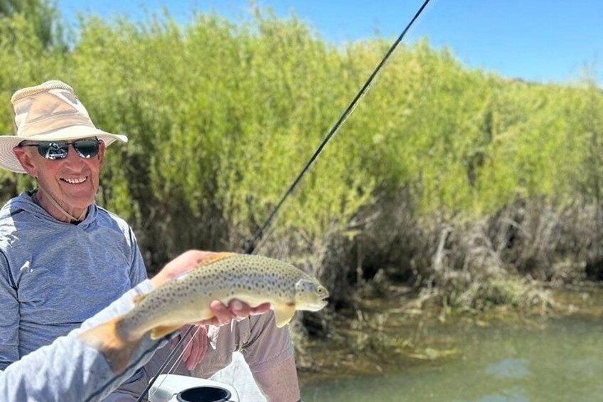A person holding a fish near a river with greenery in the background. 3