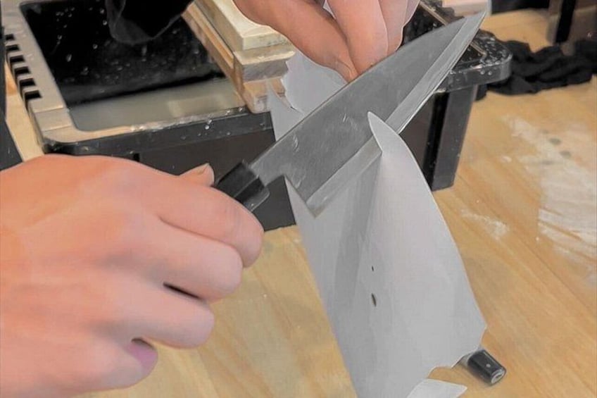 Una persona usa un coltello grande per tagliare un pezzo di tessuto bianco su un tavolo di legno. 3