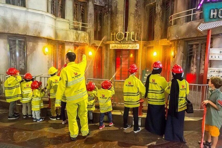 Un groupe de pompiers, vêtus d’uniformes jaunes et coiffés de casques rouges, s’est rassemblé devant un hôtel. 4