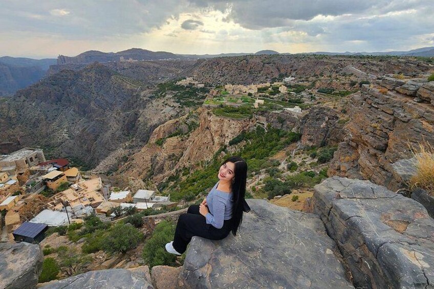 A person sitting on a rock overlooking a valley with buildings and a distant mountain. 1