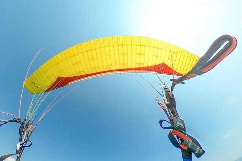 A paraglider with a yellow canopy against a clear blue sky. 2