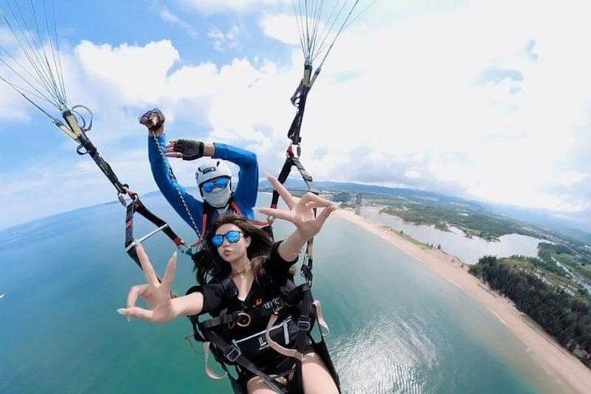 Two people paragliding over a coastal area with a beach and water visible below. 4