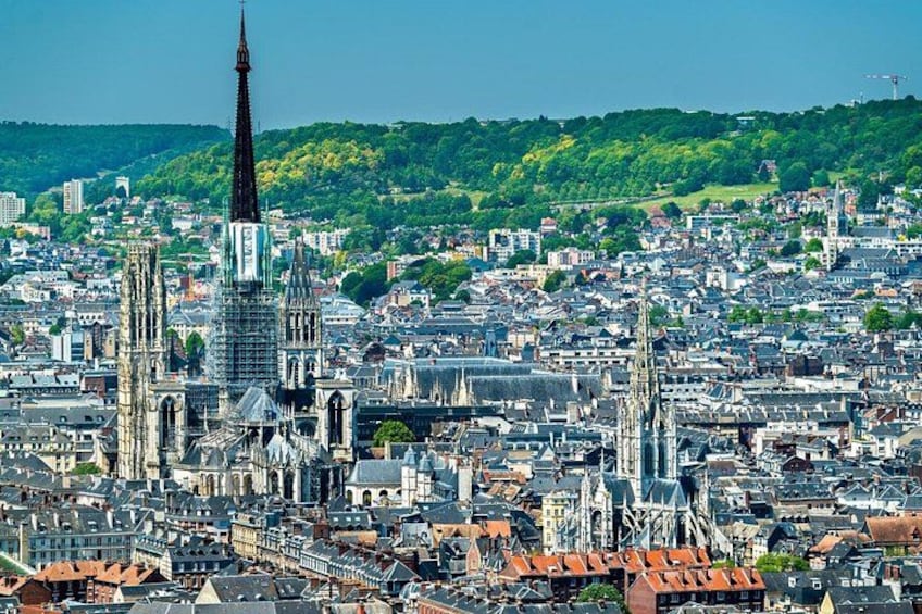 Un paisaje urbano con una catedral destacada y torres, rodeado de edificios urbanos densos y una colina verde al fondo. 1