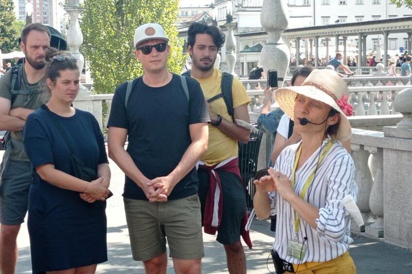 Eine Gruppe von Menschen steht auf einer Brücke mit steinernen Geländern und einem Springbrunnen im Hintergrund. 5