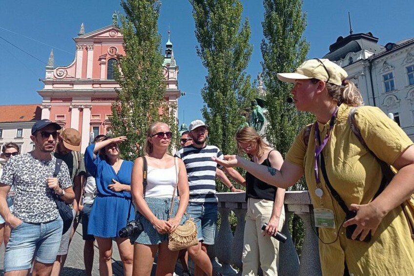 Eine Gruppe von Menschen steht auf einem öffentlichen Platz, im Hintergrund ein historisches Gebäude. 1