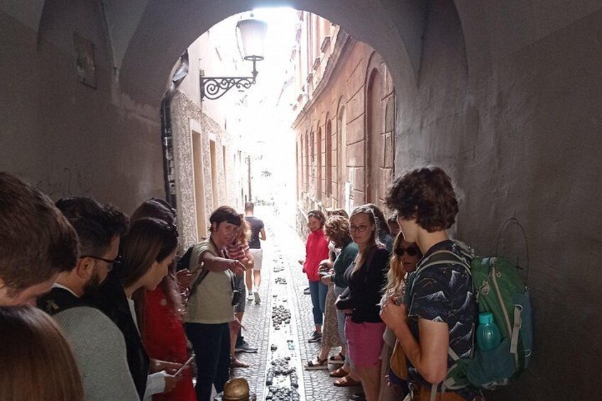 Eine Gruppe von Menschen steht in einem schmalen Gang mit Steinwänden und einer Straßenlaterne darüber. 3