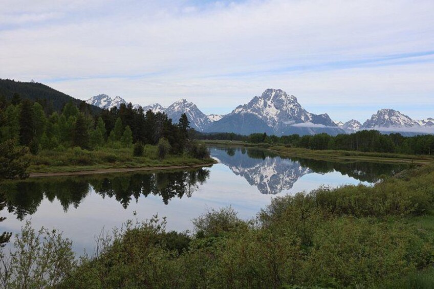 A calm lake reflecting mountains, surrounded by dense forest. 5