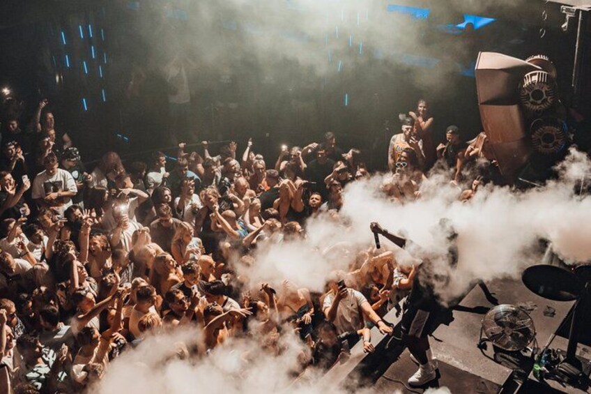 A crowded indoor event with people and smoke. 2
