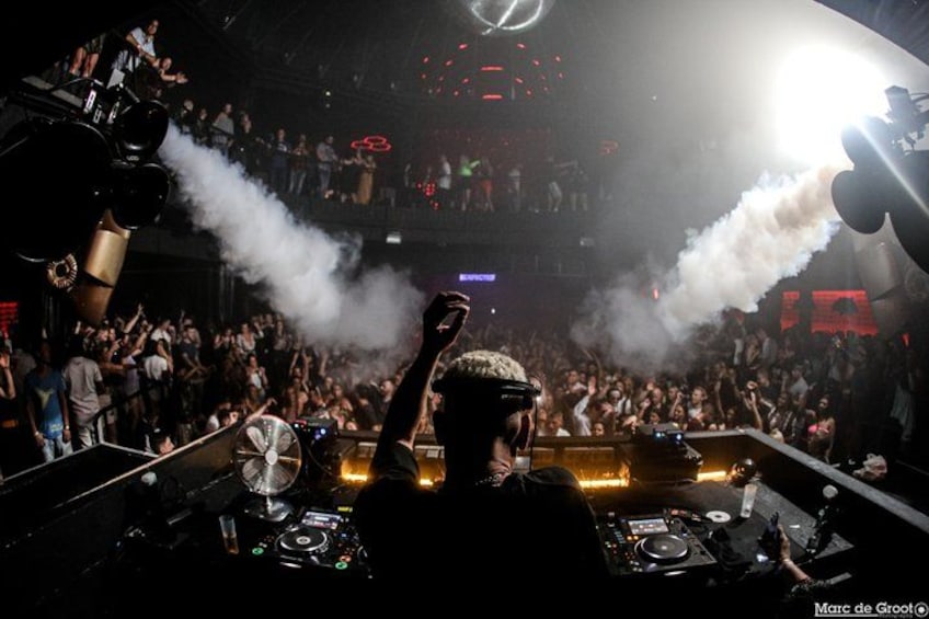 A DJ performing at a crowded event with smoke effects and a large audience. 4