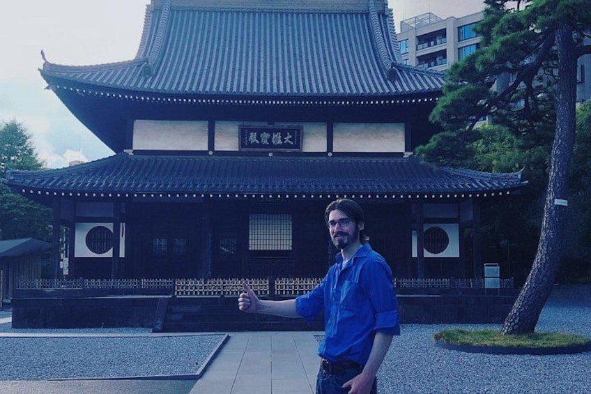 En person står foran en traditionel japansk bygning med et tagtækket tag og en skilteplade. 3