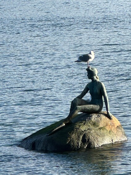 A statue of a seated figure on a rock with a seagull perched on its head. 4