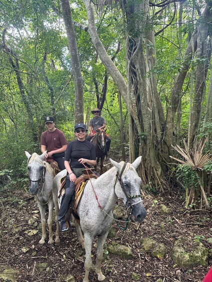 Three people riding horses in a forested area with dense trees and foliage. 2
